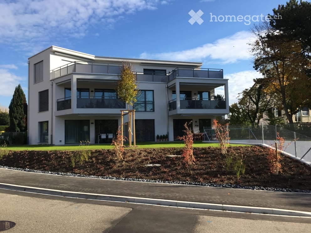 Modern two-story house with large windows, balconies, and a landscaped front yard.