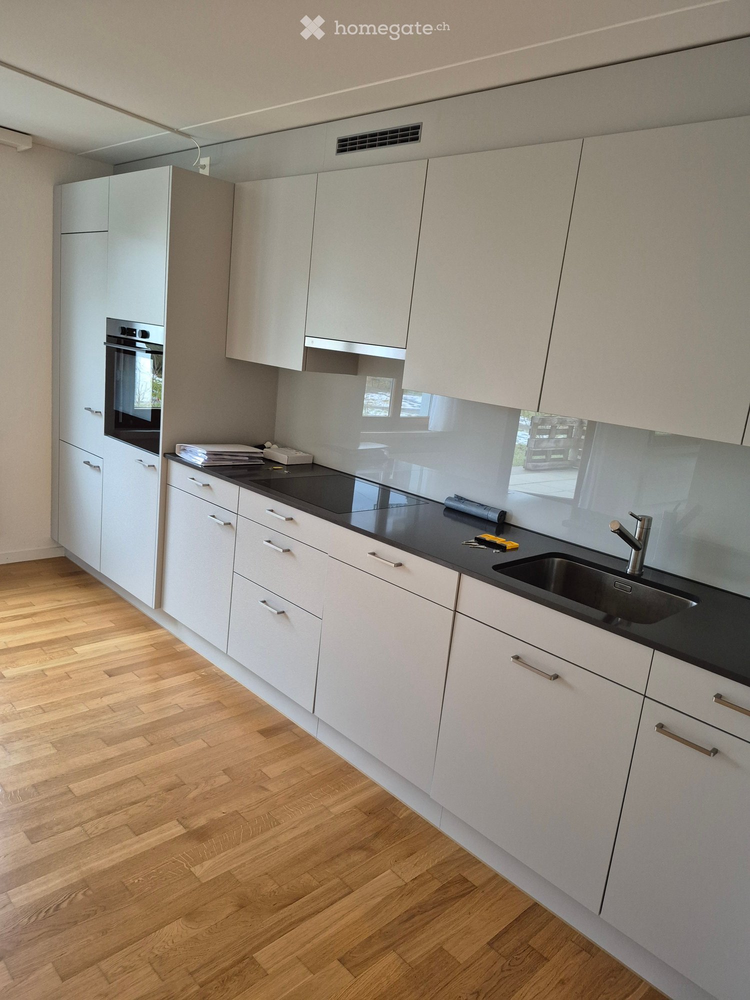 Modern kitchen with white cabinets, black countertop, stainless steel sink, and built-in oven. Wooden flooring and sleek design.