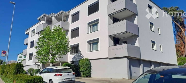 Modern multi-story apartment building with balconies, white exterior, and several windows.