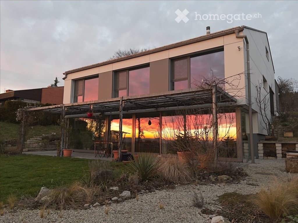 Modern two-story house with large windows, a covered outdoor patio, and a scenic sunset view.