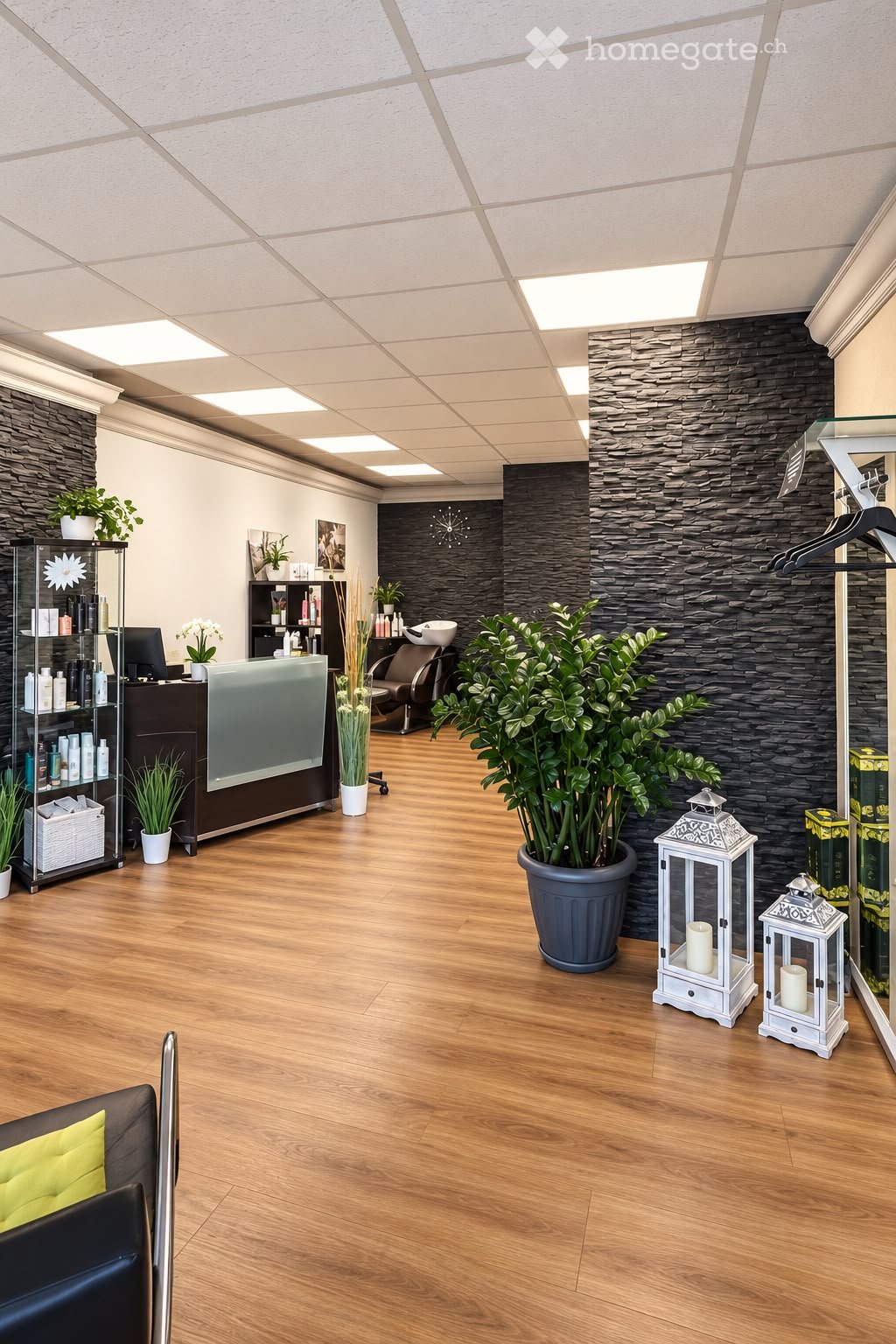 Modern, well-lit reception area with wooden flooring, a sleek reception desk, a black leather chair, decorative plants, and two white lanterns.
