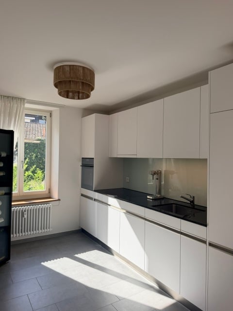 Modern kitchen with white cabinets, black countertop, stainless steel sink, and a window with a view of greenery.