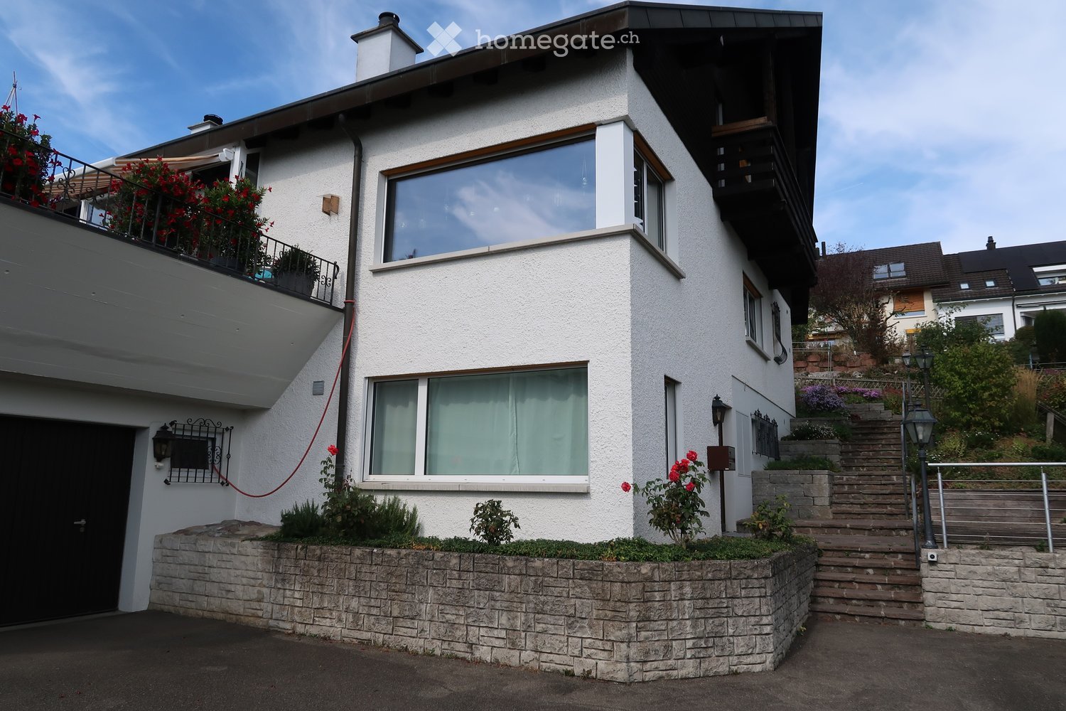 Two-story house with white exterior, large windows, balcony, and garden area with steps leading up.