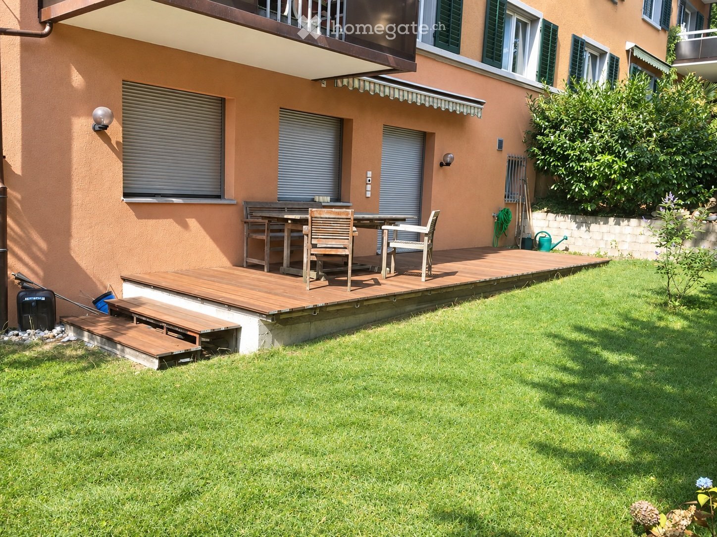 Wooden patio with a table and chairs, surrounded by a well-maintained lawn and garden area.
