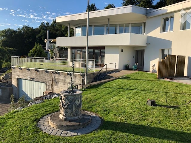 Modern two-story house with white exterior, large windows, balcony, garage, and well-maintained lawn.