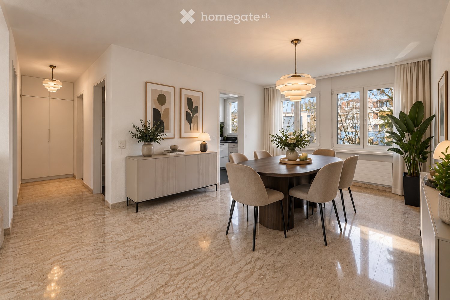 Modern dining room with a round wooden dining table surrounded by six chairs, a sideboard with a vase and books, large windows with curtains, and decorative artwork on the walls.