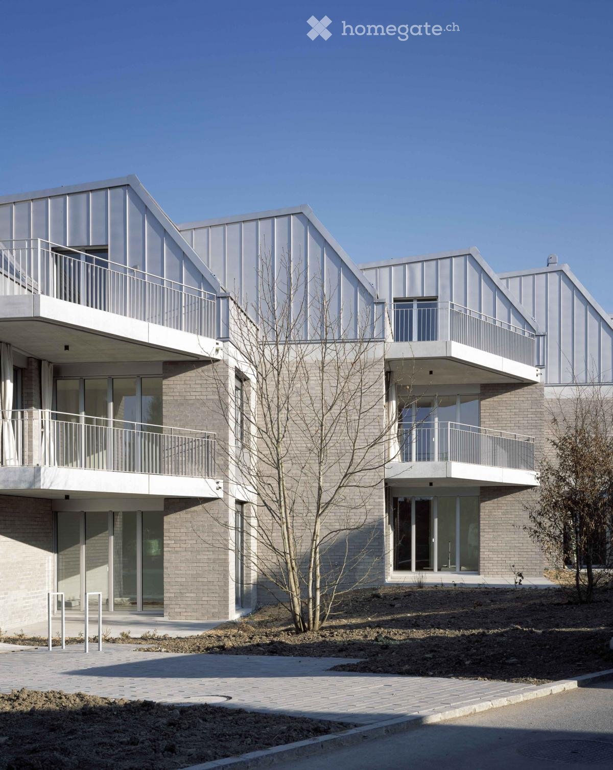 Modern two-story building with a combination of metal and brick facades, large glass windows, and balconies with white railings.