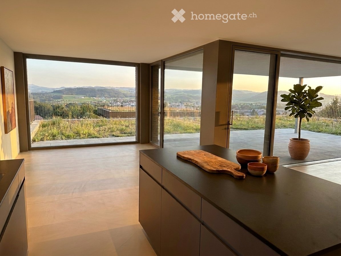 Modern kitchen with large windows offering a scenic view, dark countertops, and wooden cutting board with bowls on display.