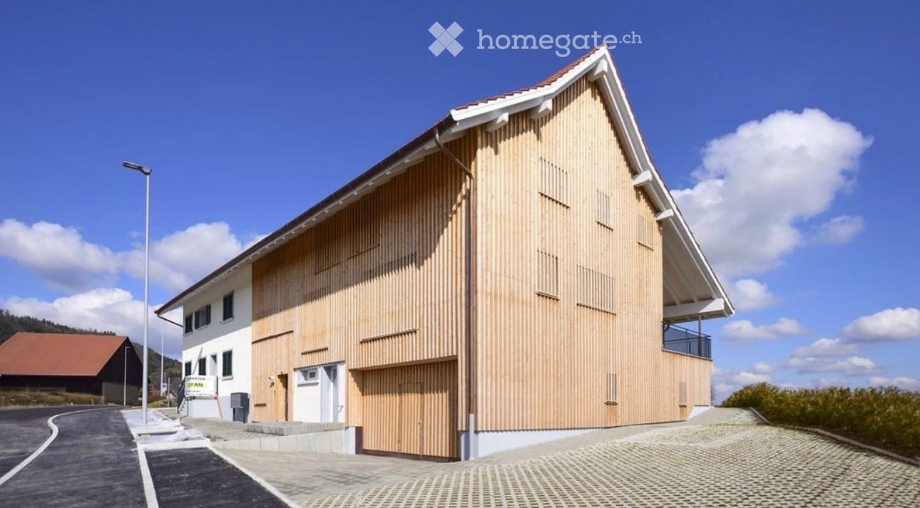 Modern two-story building with a wooden facade and white trim, featuring a garage and a balcony on the upper level.