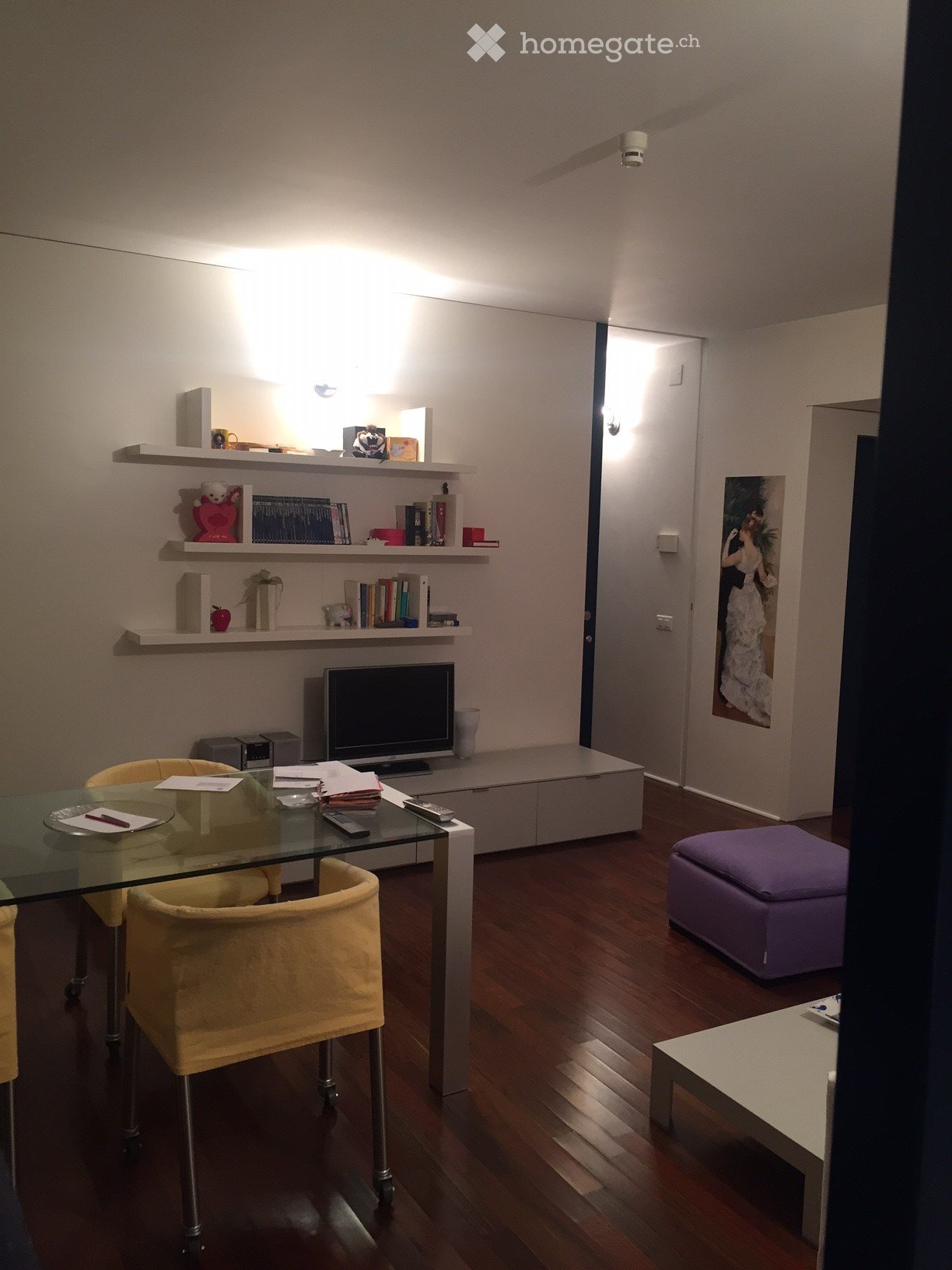 A modern living room with wooden flooring, a glass dining table with yellow chairs, a purple ottoman, shelves with books and decorative items, and a television set.