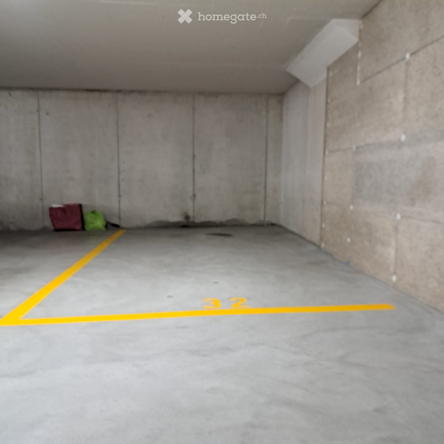 Empty underground parking space with concrete walls and floor, marked parking spot number 32, and two bags placed against the wall.