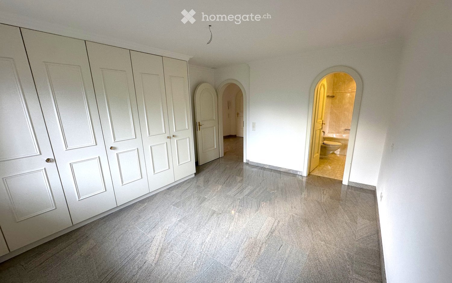 Empty room with light-colored walls, large built-in wardrobe, and two arched doorways leading to other spaces.