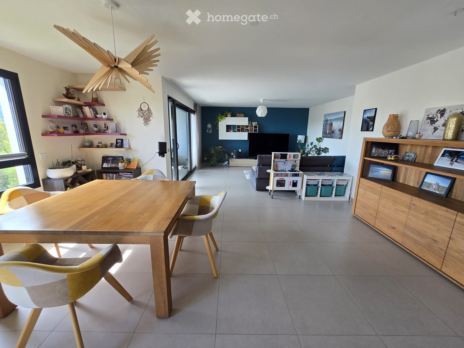Open-plan living and dining area with modern furniture, large windows, and decorative shelves.