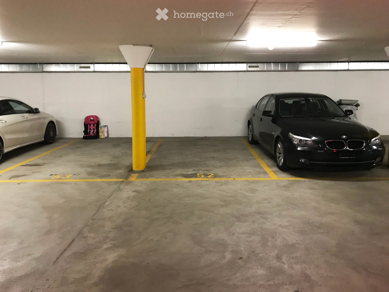 Underground parking area with two parked cars, marked parking spaces, and a central support column.