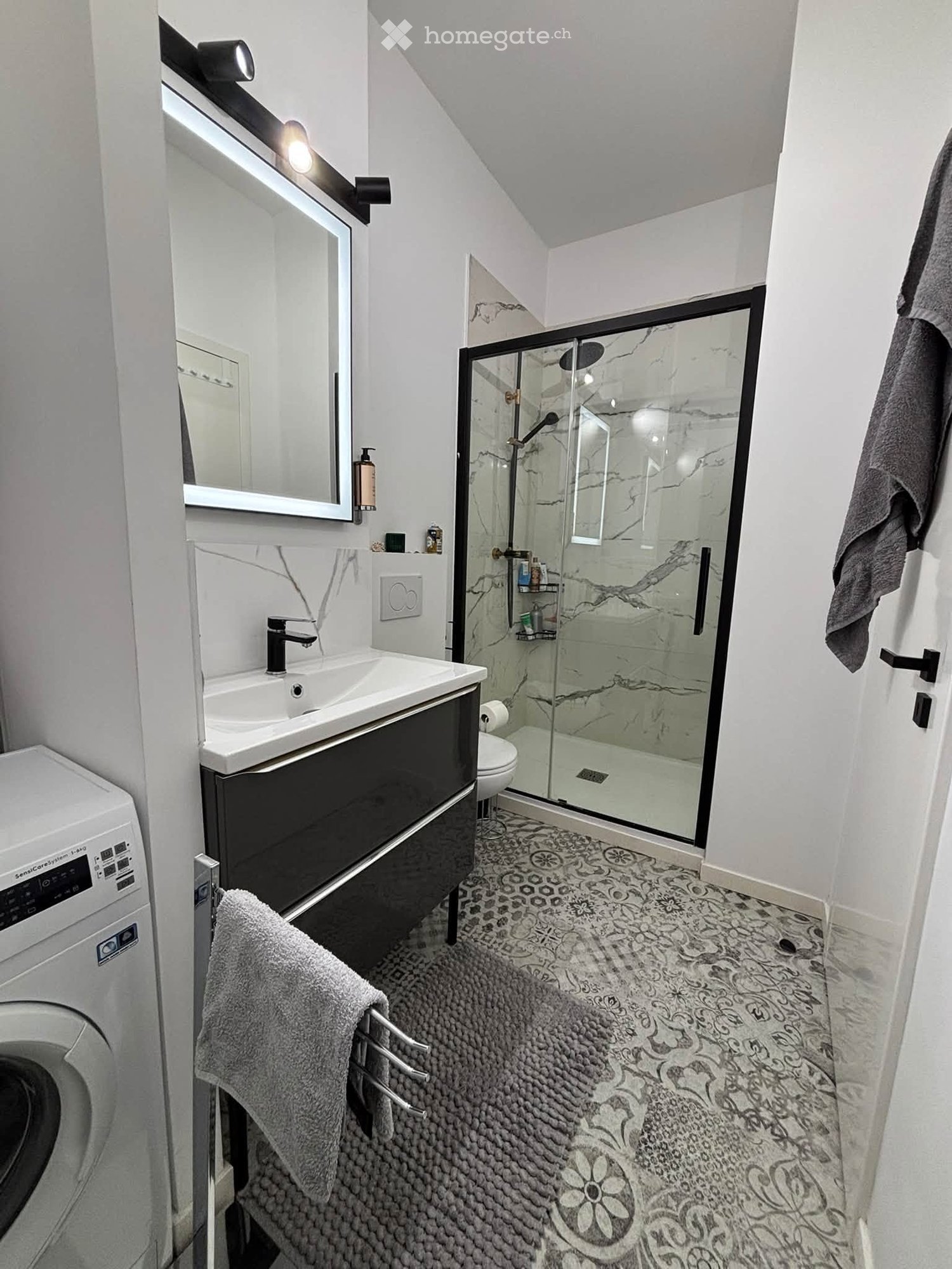Modern bathroom with a black vanity, white sink, large mirror, glass-enclosed shower, and decorative tile floor.