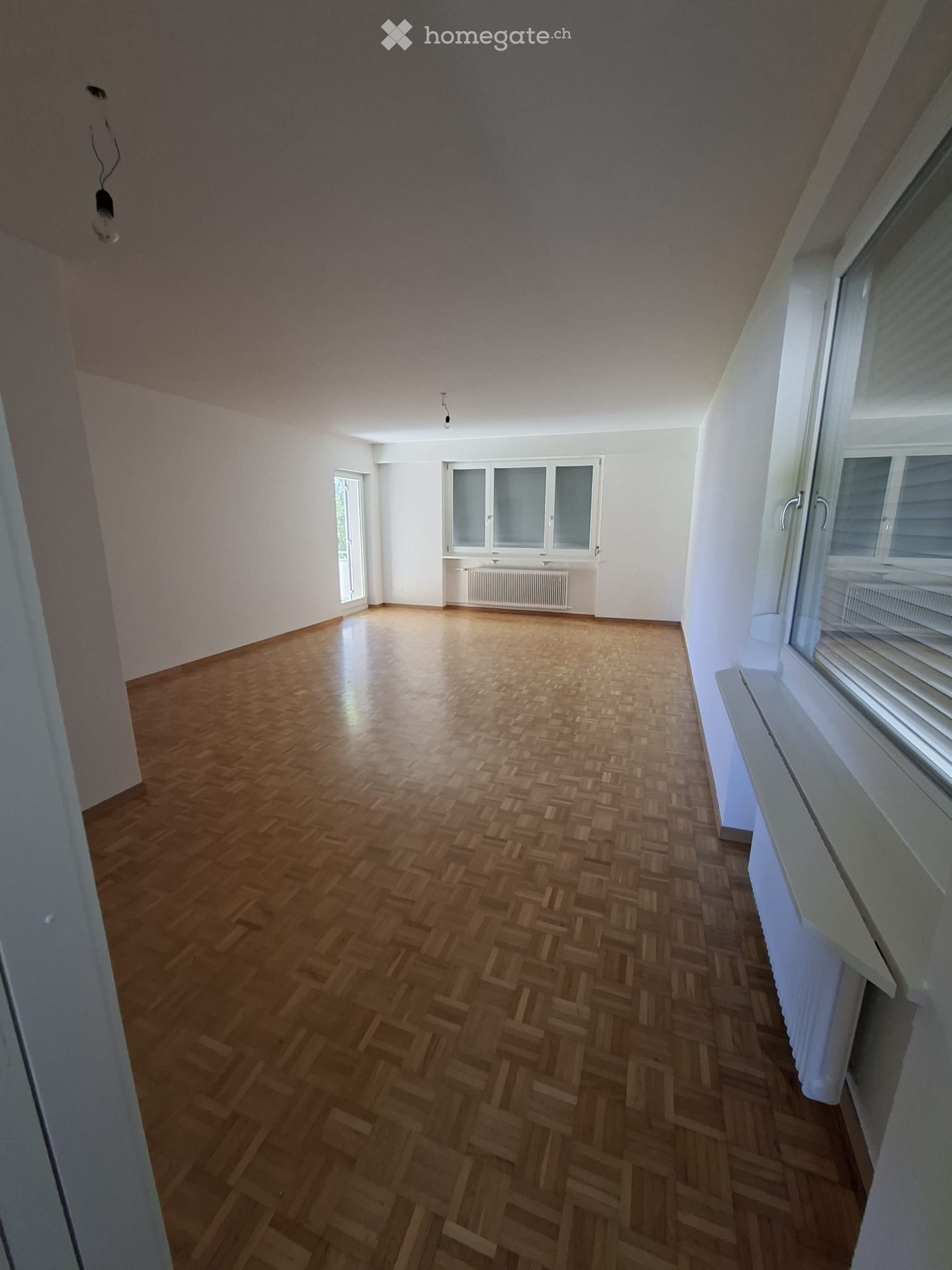 Empty room with wooden herringbone flooring, white walls, and multiple windows with blinds. No furniture or equipment present.