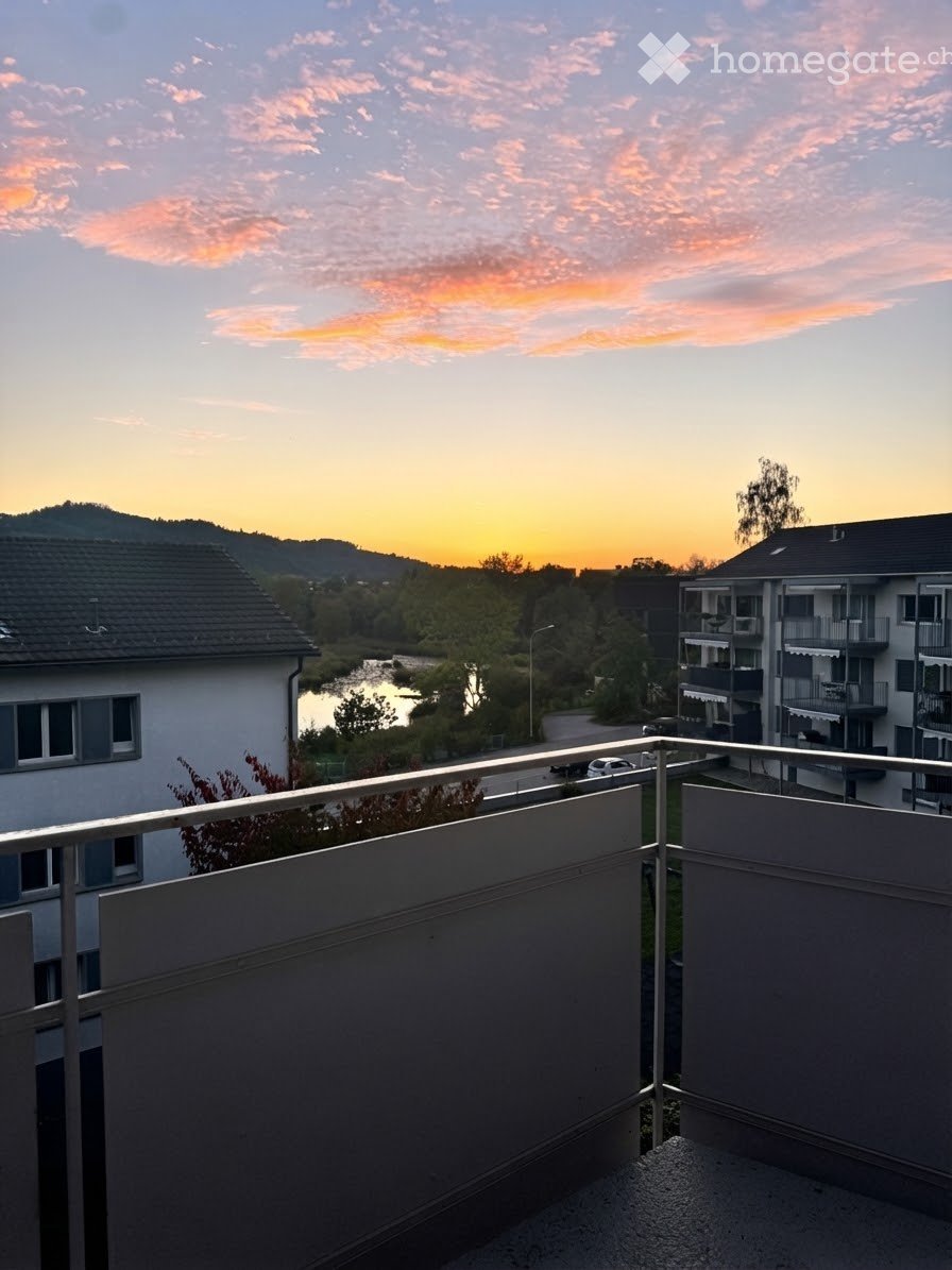 Balcony overlooking a scenic view of a river, surrounding buildings, and a sunset sky.