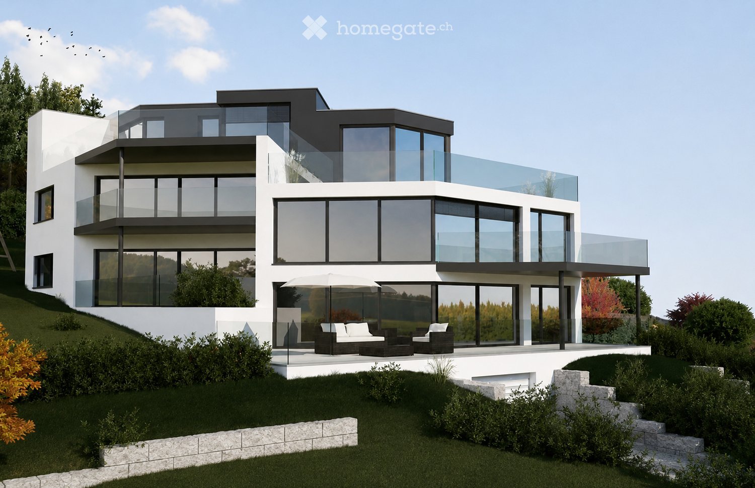Modern two-story house with white and black exterior, large glass windows, and a raised ground floor. Features include a balcony, outdoor seating area with a sofa and chairs, and a well-maintained garden.