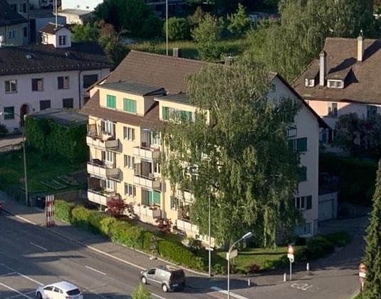 Multi-story residential building with multiple apartments, balconies, and surrounding greenery.