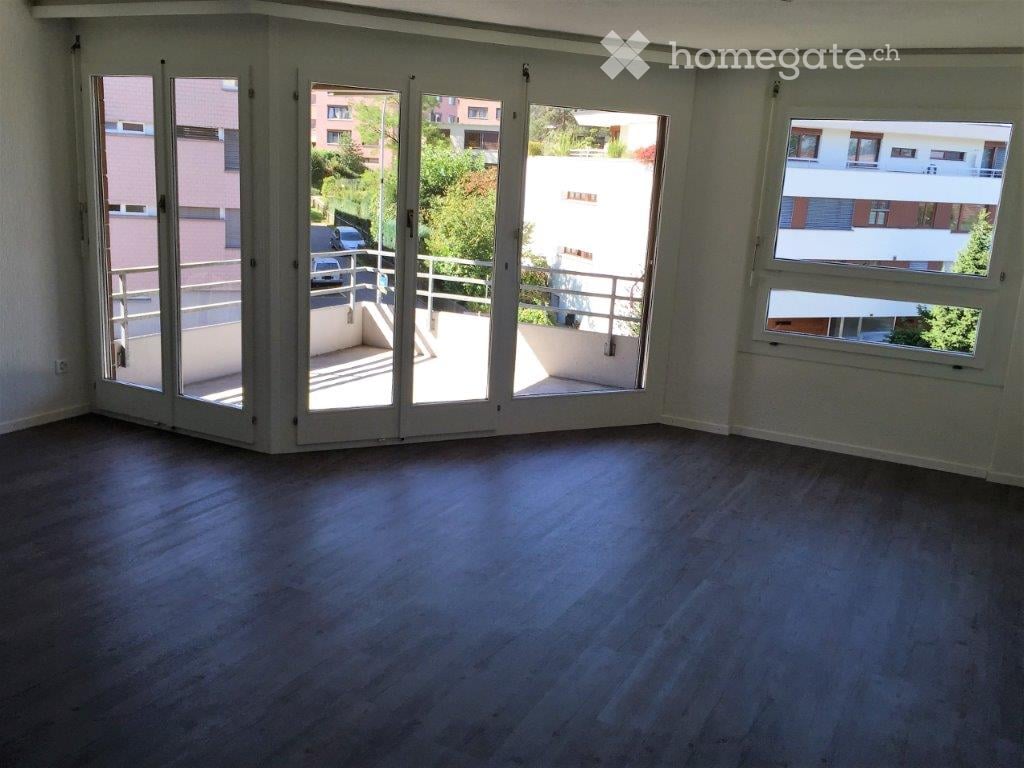 Empty room with wooden flooring, large sliding glass doors leading to a balcony, and a view of the surrounding area.