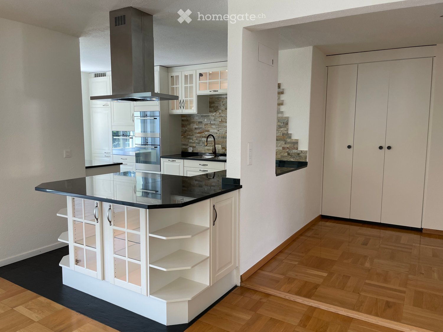 Modern kitchen with white cabinets, black countertops, island with glass panels, stainless steel appliances, and wooden flooring.