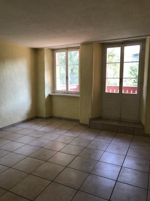 Empty room with tiled floor, two windows, and a small step leading to an outdoor area.