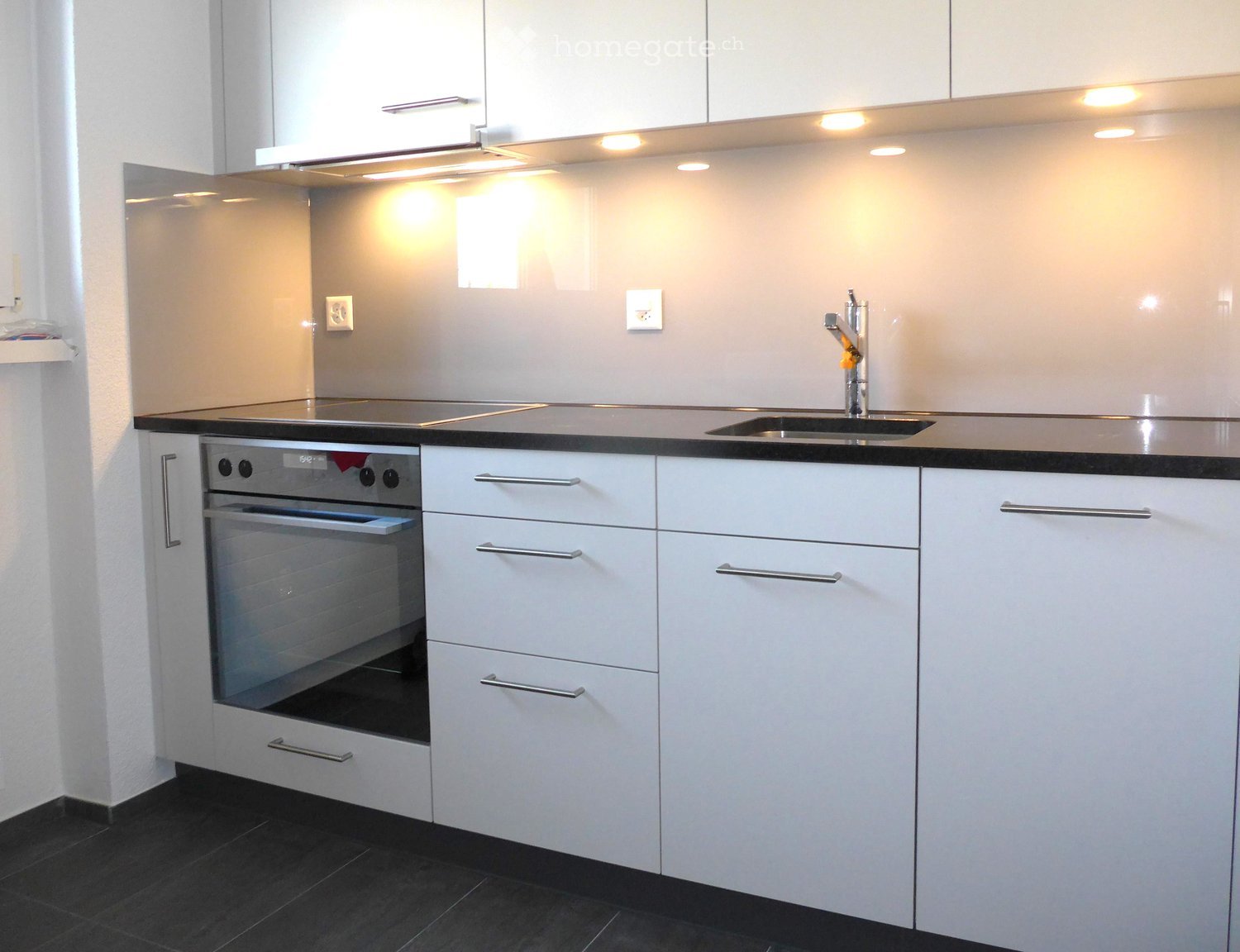 Modern kitchen with white cabinets, stainless steel oven, sink, and faucet, illuminated by recessed lighting.