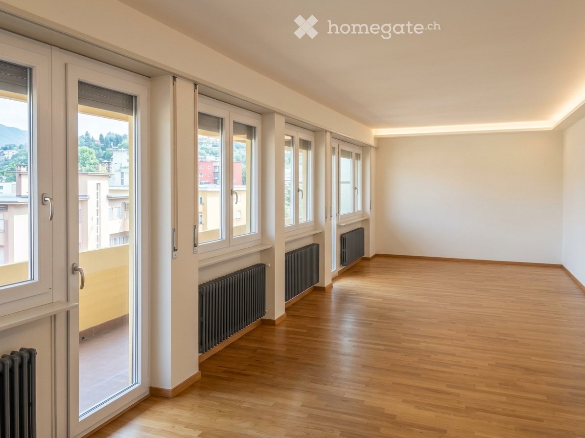 Empty room with wooden flooring, large windows, radiators, and a view of the city and mountains.