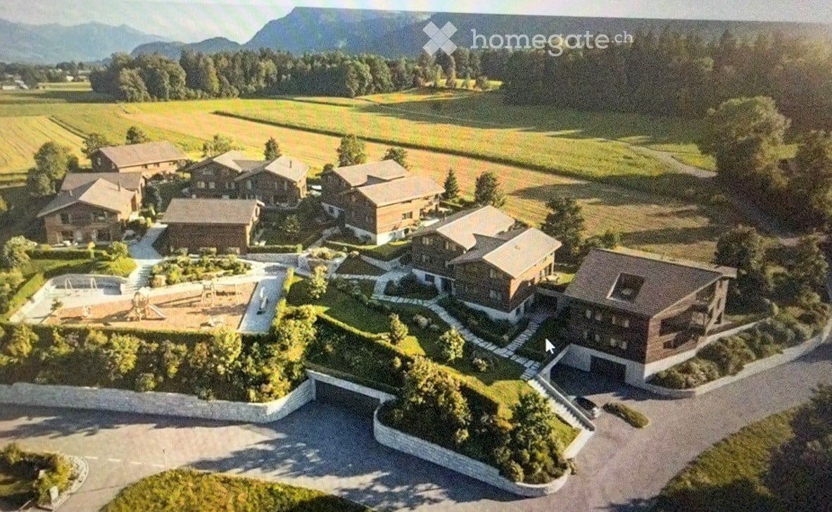 Aerial view of a residential complex with multiple houses, a swimming pool, and a garage, surrounded by greenery and a scenic mountain backdrop.