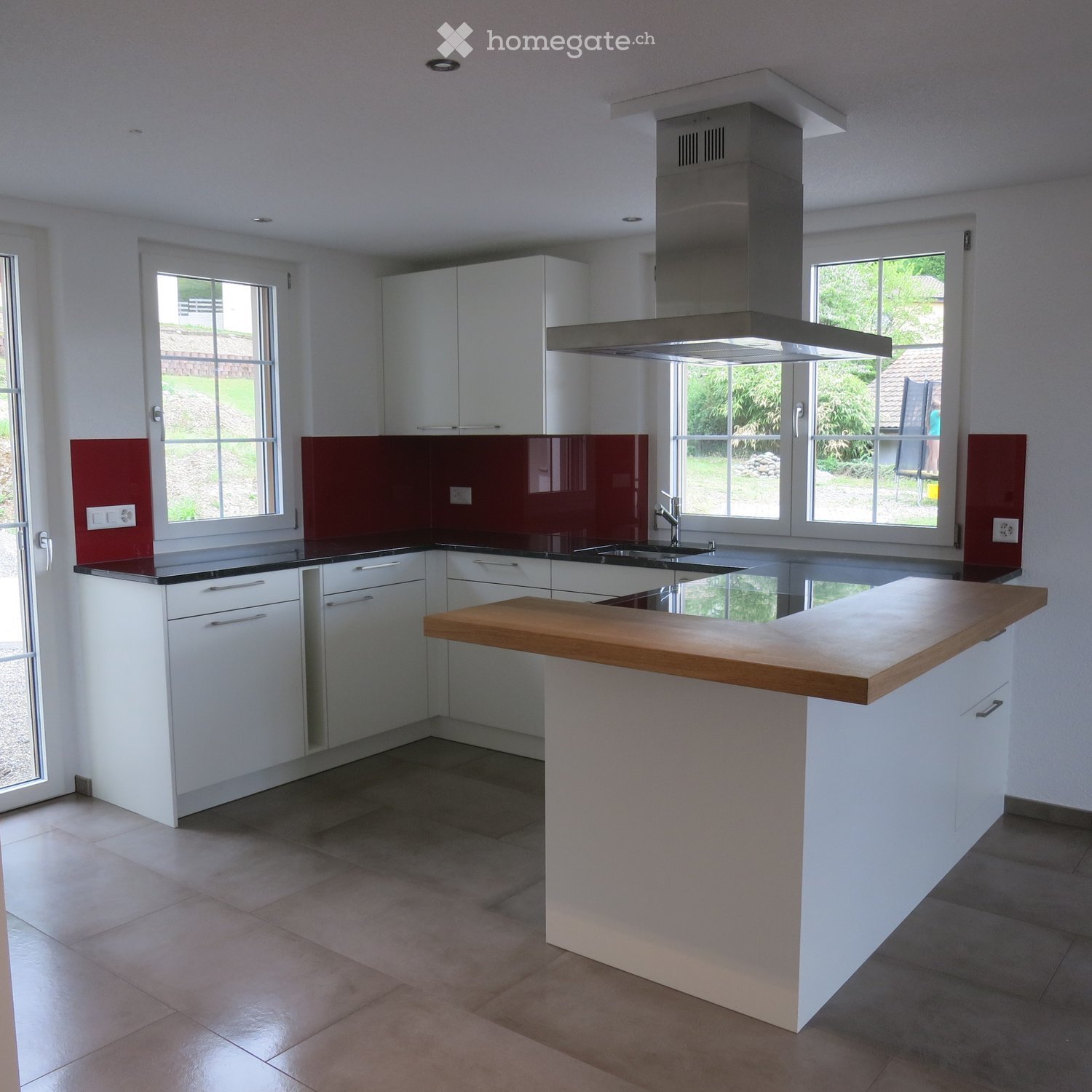 Modern kitchen with white cabinets, a wooden island, stainless steel sink, and red backsplash.