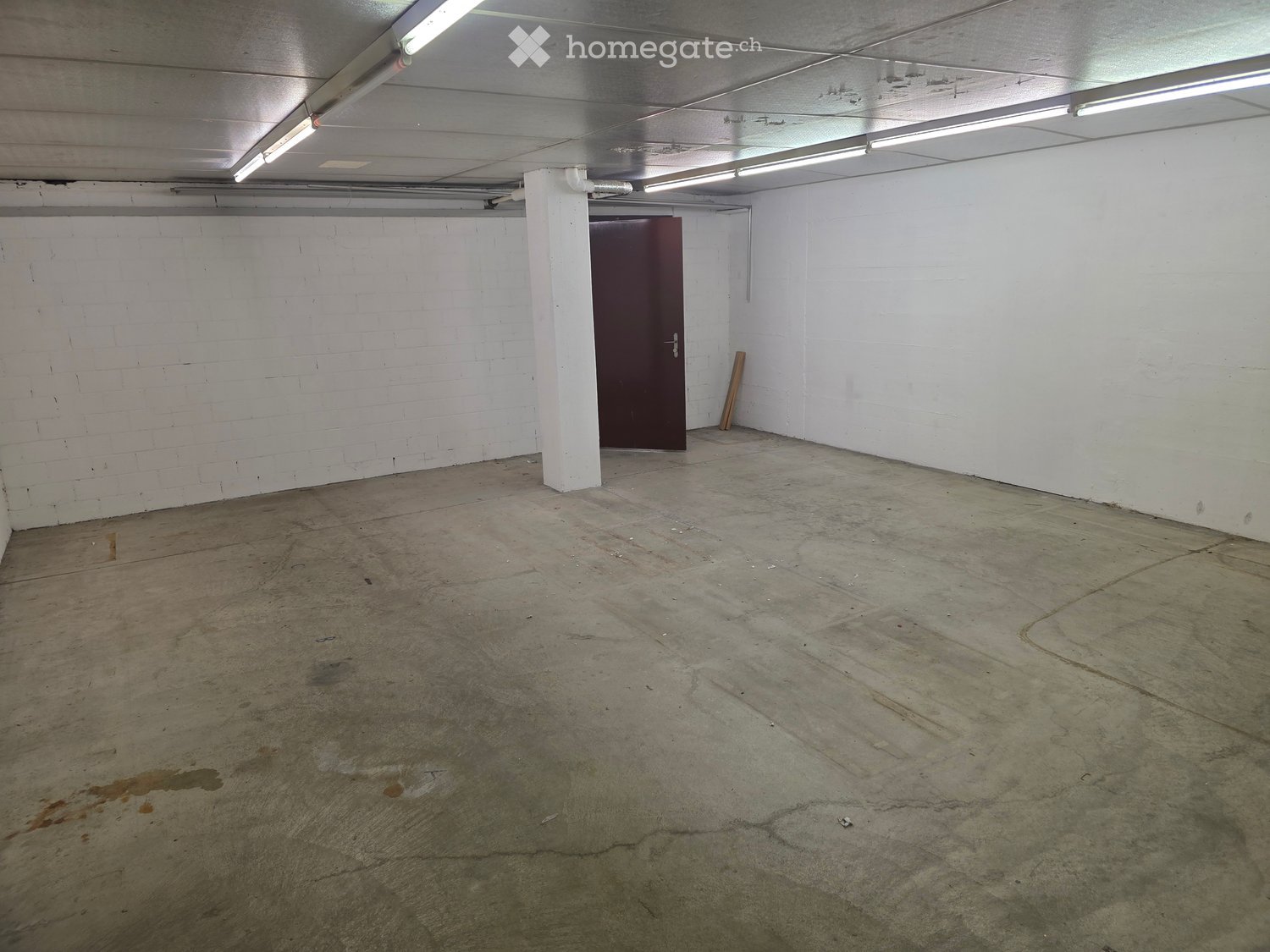 Empty room with concrete floor, white brick walls, and a single door. No furniture or equipment present.