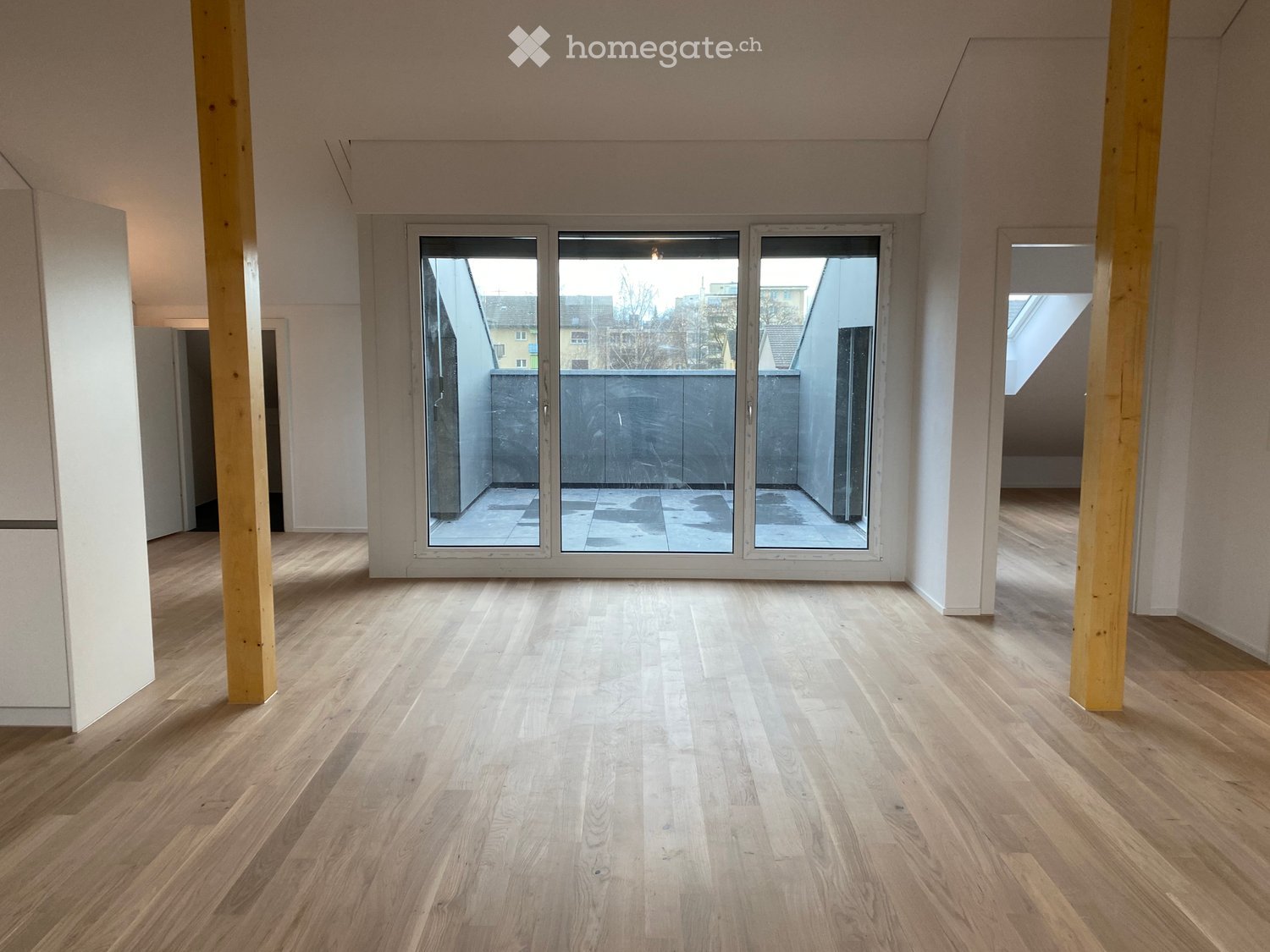 Empty room with light wooden flooring, white walls, and large glass sliding doors leading to a balcony area.