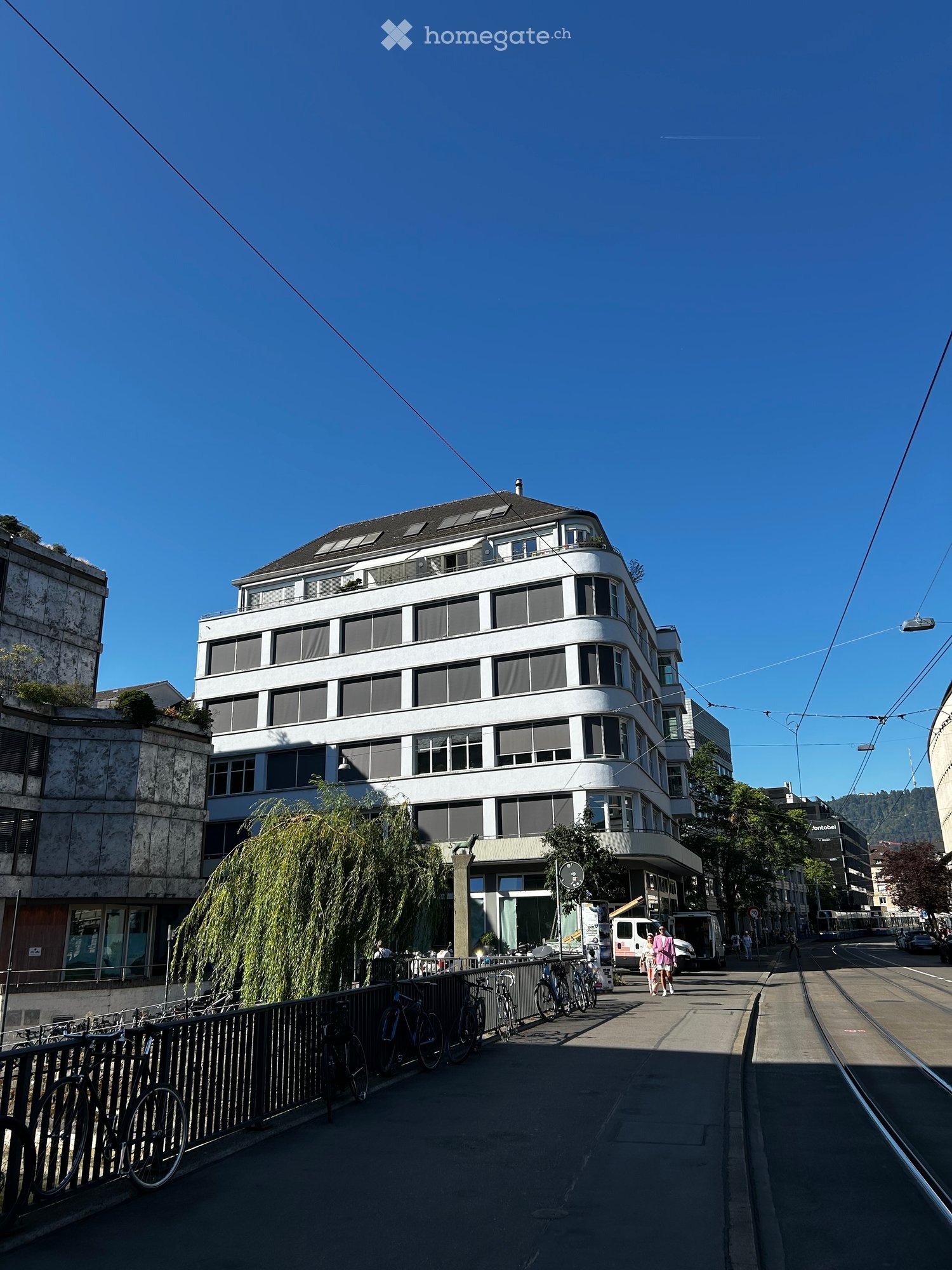 Modern multi-story building with large windows and a curved facade, located on a street with bicycles parked along the sidewalk.
