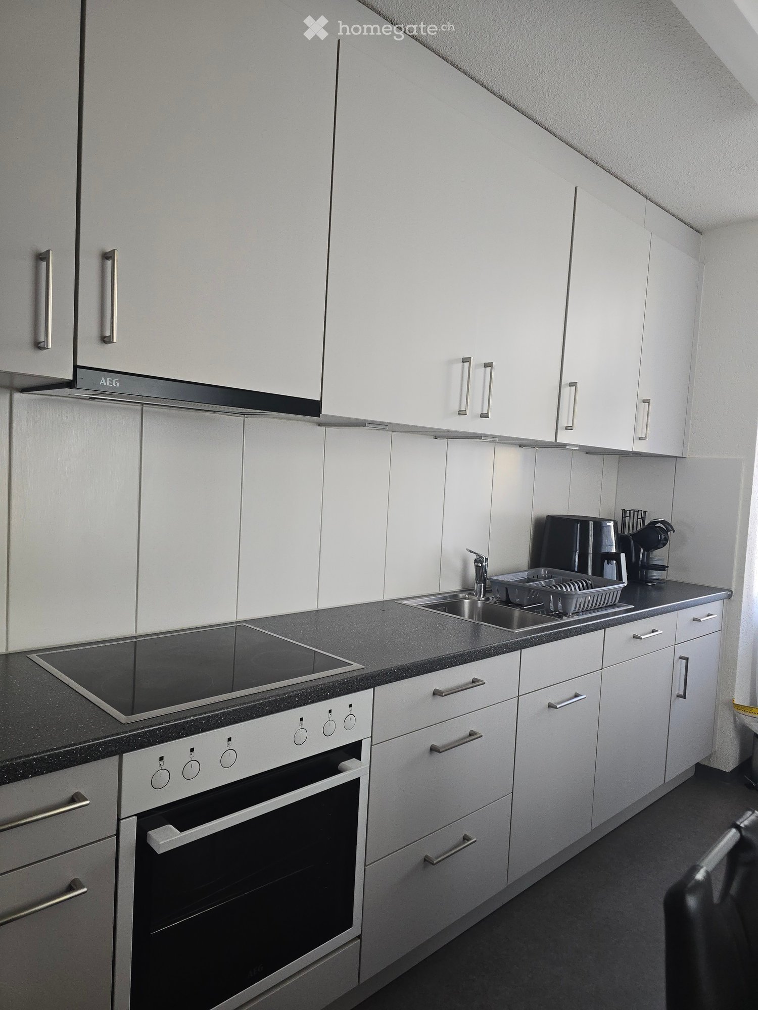Modern kitchen with white cabinets, stainless steel appliances, and a black countertop. Features an induction cooktop, oven, sink, and coffee maker on the counter.