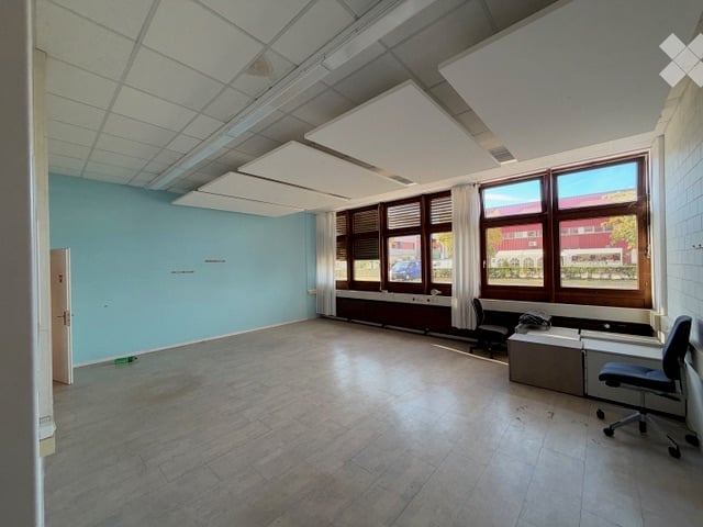 Empty room with light blue walls, large windows with blinds, and a tiled floor. No furniture or equipment present.