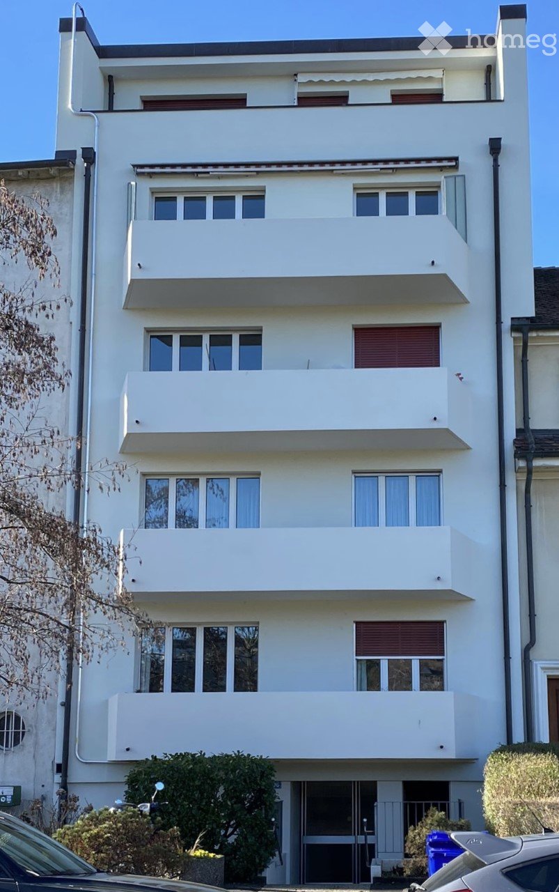 Four-story white building with multiple balconies and large windows, featuring a modern architectural style.