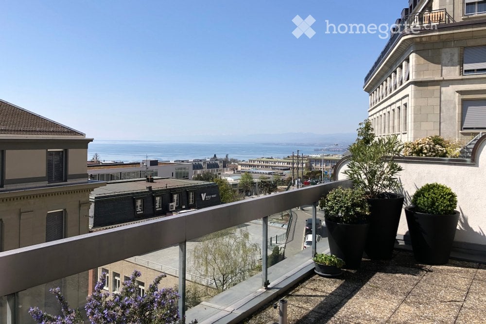 Balcony with a panoramic view of the sea and cityscape, featuring potted plants and a modern glass railing.