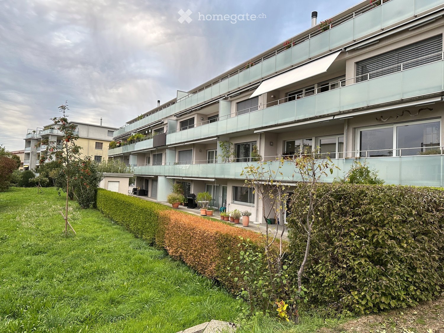Modern multi-story residential building with balconies, large windows, and surrounding greenery.