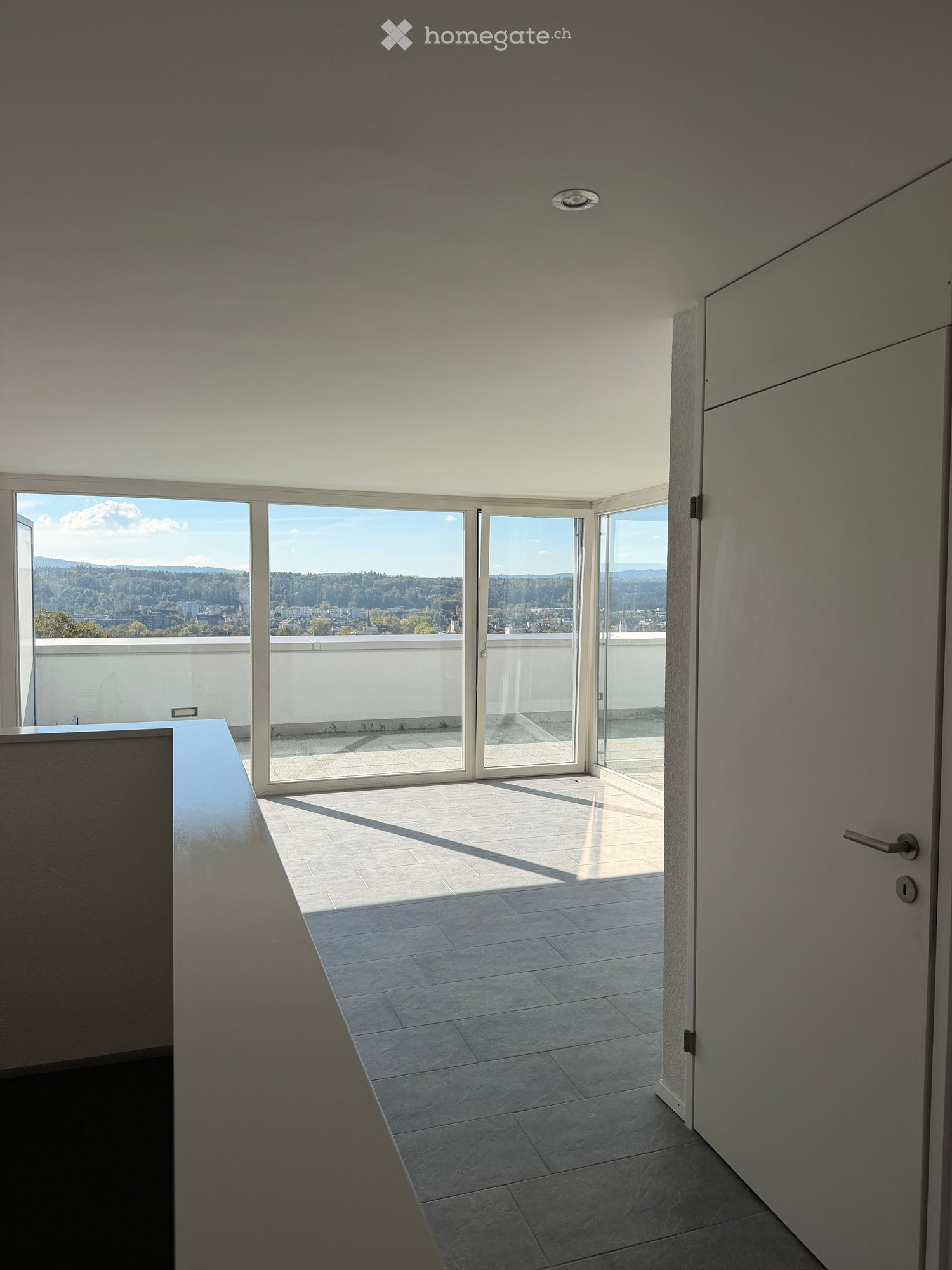 Modern hallway with large glass doors leading to a balcony, tiled floor, and minimalistic design.