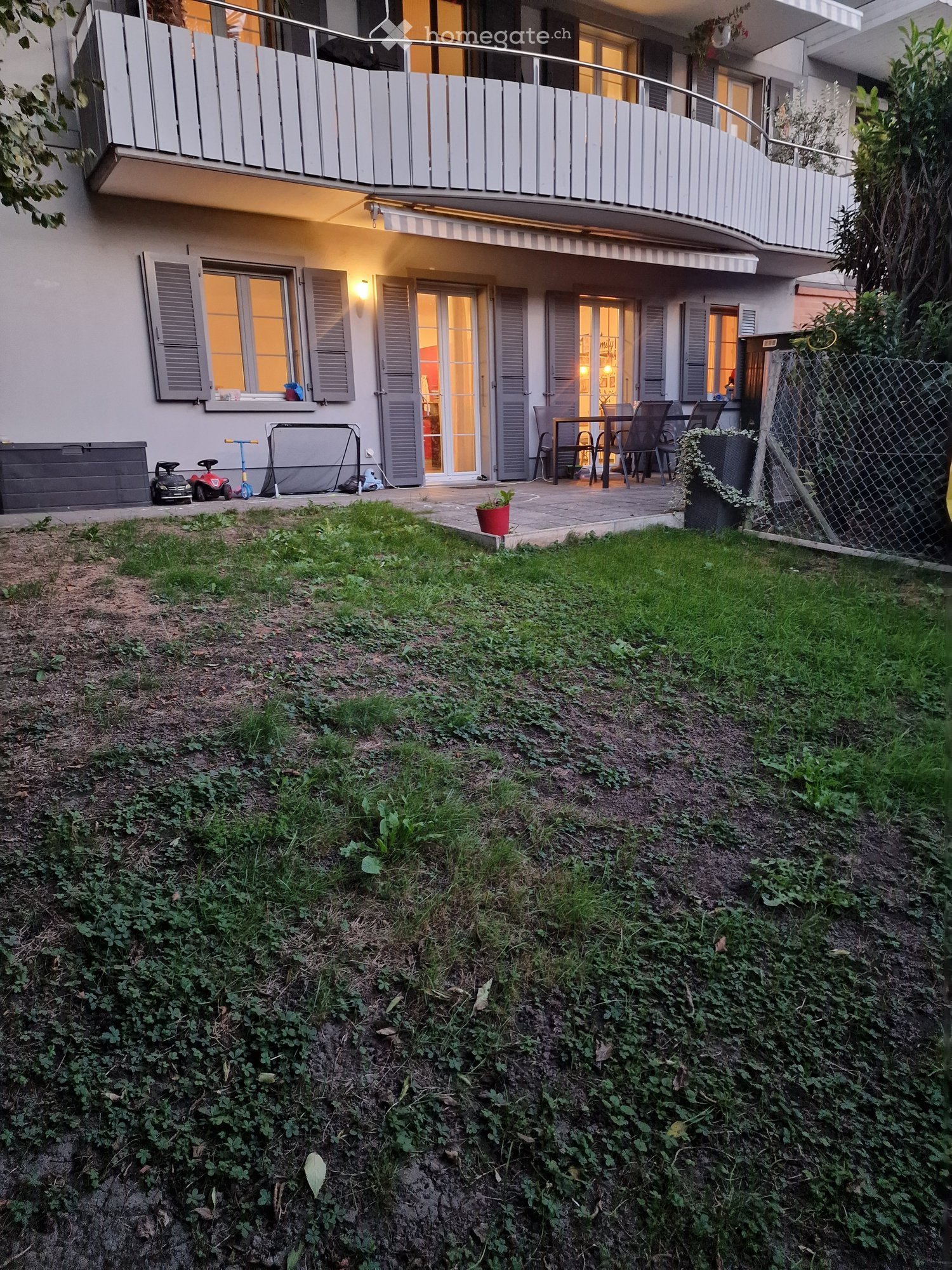 Garden area with a raised ground floor, a small patio with outdoor furniture, and a grassy slope covered in plants and vines.