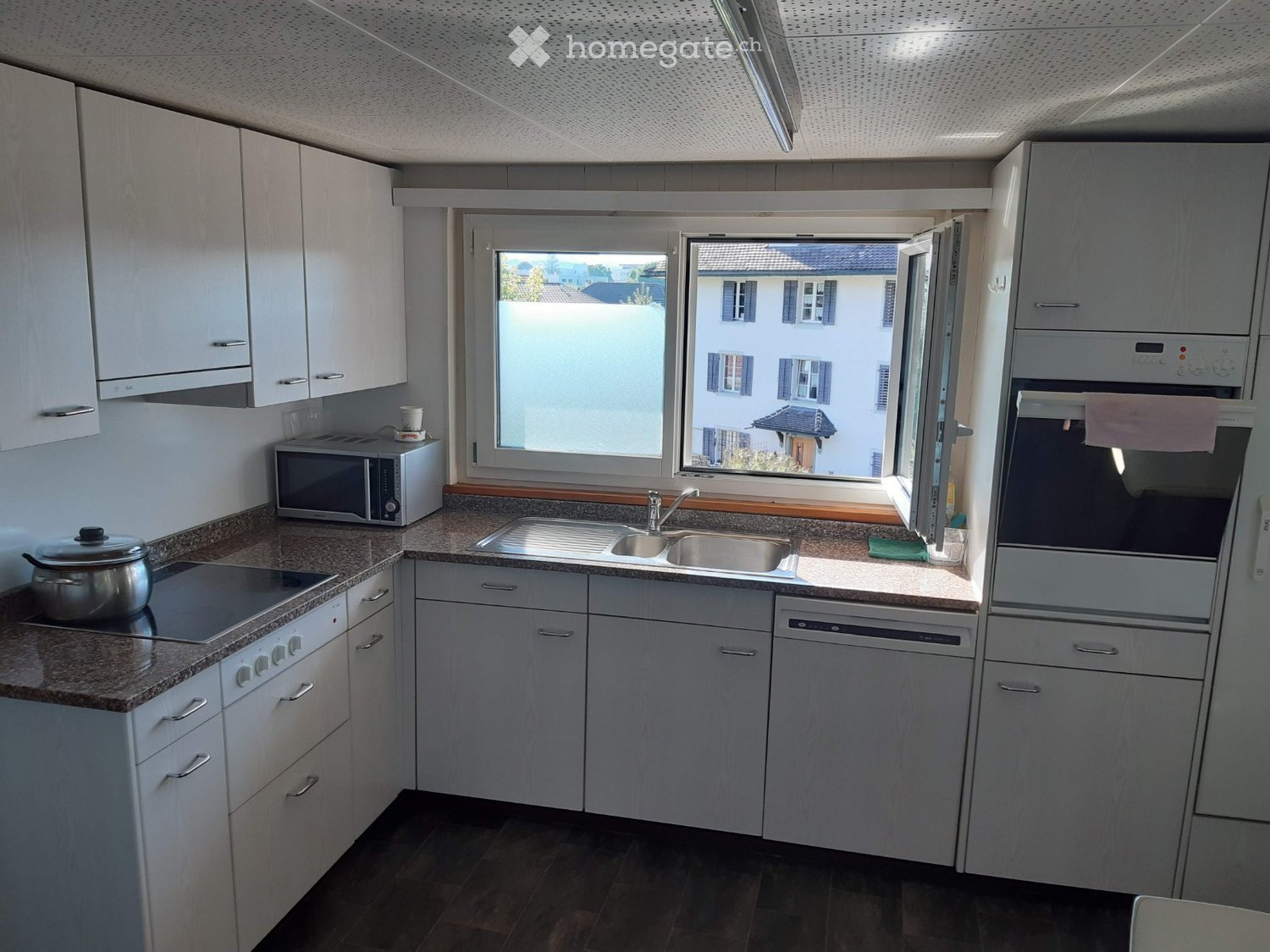 Modern kitchen with white cabinets, granite countertops, stainless steel appliances, and a large window overlooking a residential area.