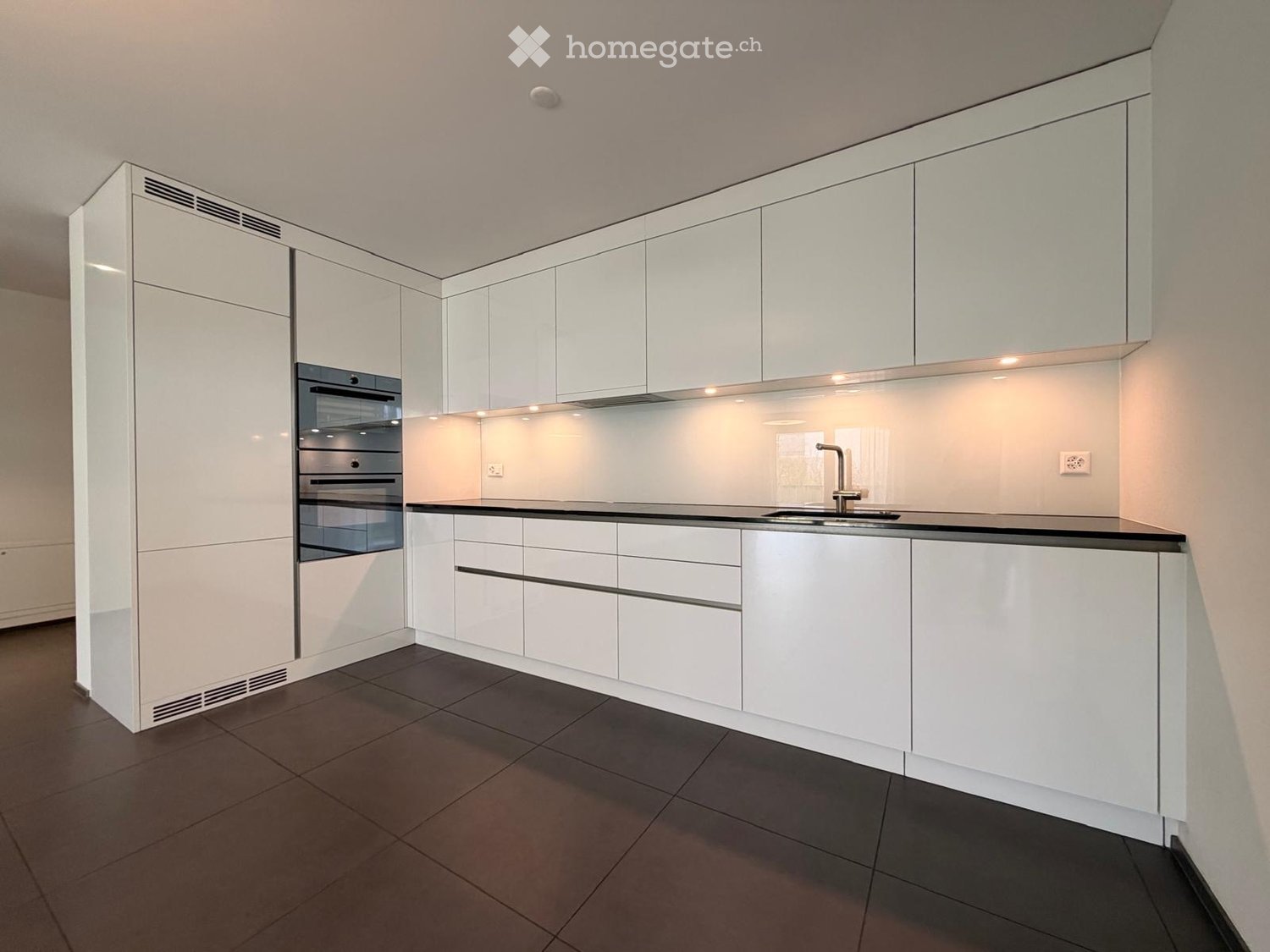 Modern kitchen with white cabinets, black countertop, stainless steel sink, and built-in oven.
