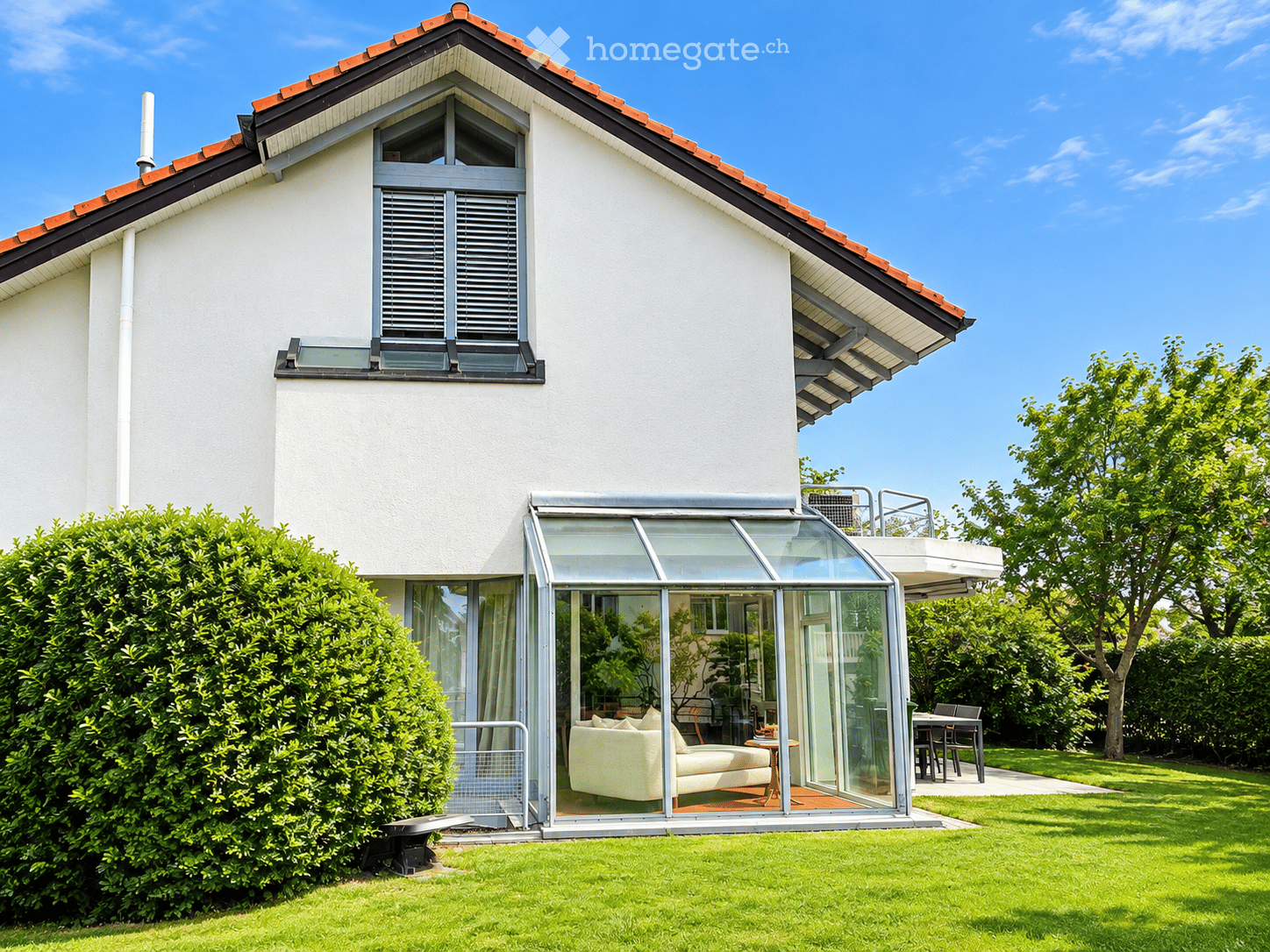 Two-story house with white exterior, red-tiled roof, large glass extension, and well-maintained garden.