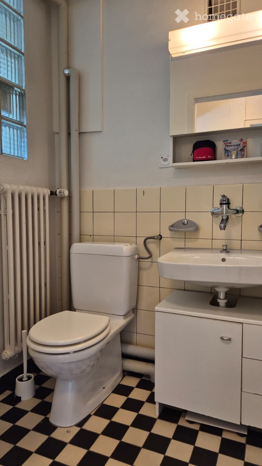 Bathroom with a toilet, sink, faucet, cabinet, radiator, mirror, and shelf. The floor has a black and beige checkered pattern.