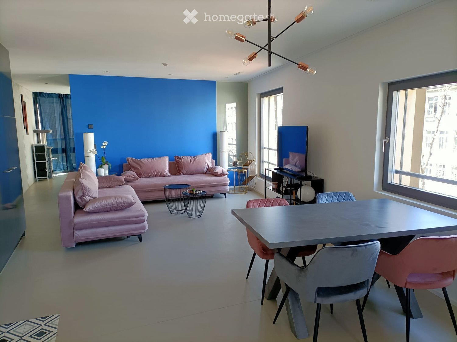 Modern living room with a pink sofa, dining table, chairs, and a large window with a view.