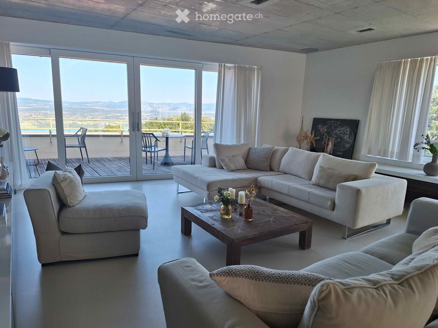 Modern living room with large windows and a view, featuring a sectional sofa, coffee table, and outdoor seating area.