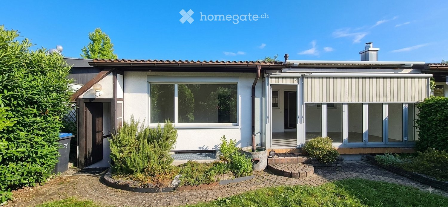 Single-story house with white exterior, large windows, covered entrance, and well-maintained garden.
