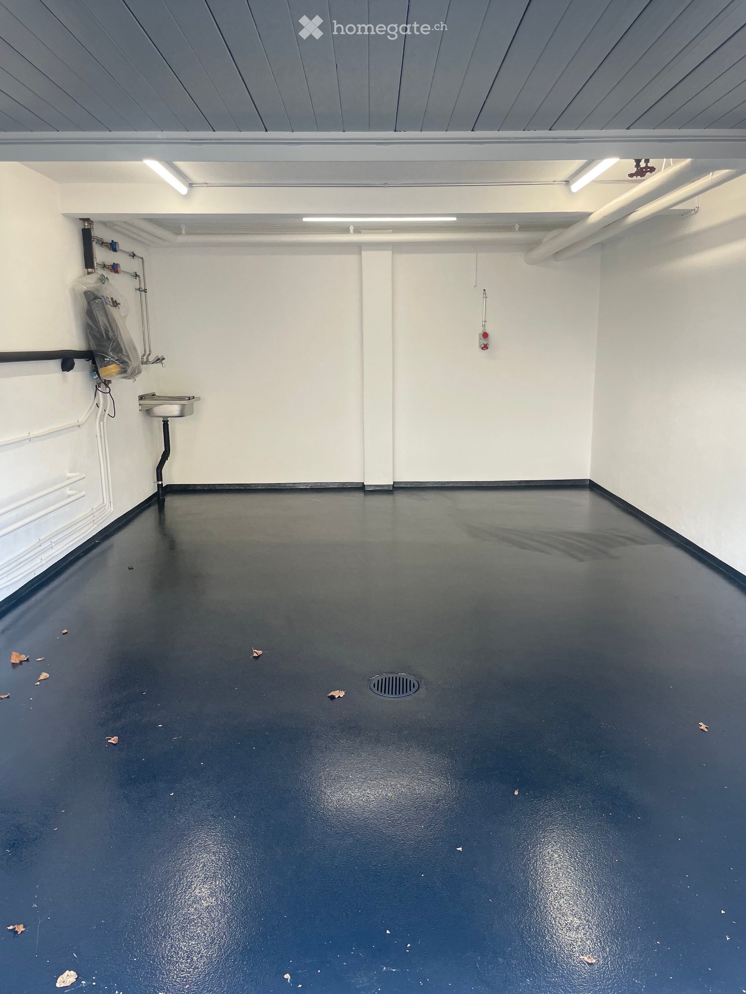 Empty room with white walls, black floor, and a small sink in the corner. No furniture or equipment present.