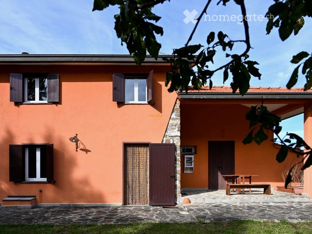 Two-story orange building with black shutters, stone patio, and a wooden bench outside