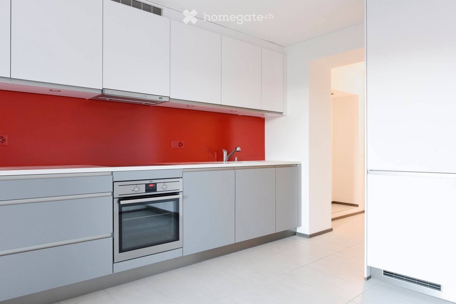 Modern kitchen with white cabinets, stainless steel oven, and a red accent wall. The space includes a sink with a modern faucet and a built-in oven with a digital display.